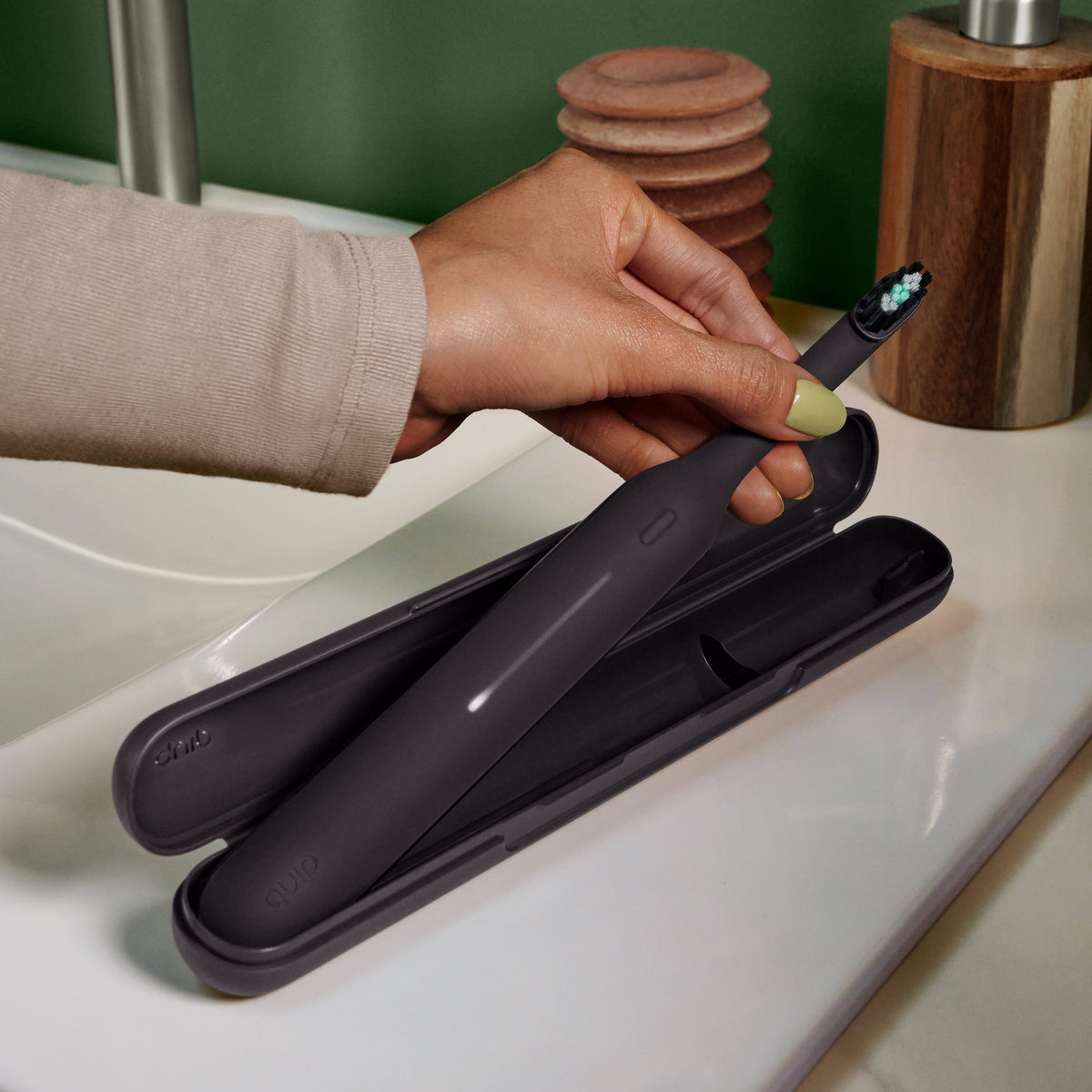 Ultra™ Travel Case holding a sleek black electric toothbrush, shown open on a bathroom counter as a hand lifts the toothbrush from the protective case.
