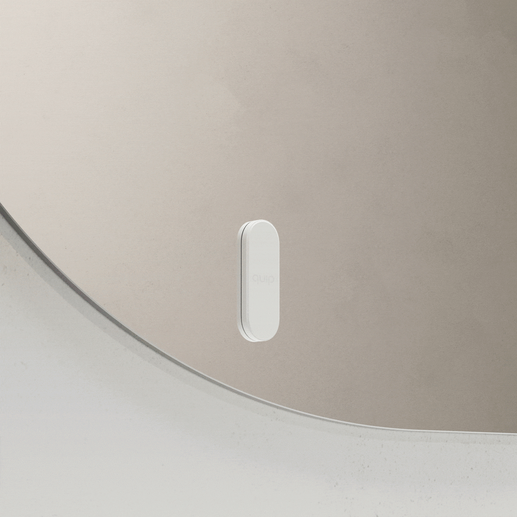 White quip toothbrush mount attaching to and releasing from a bathroom mirror.