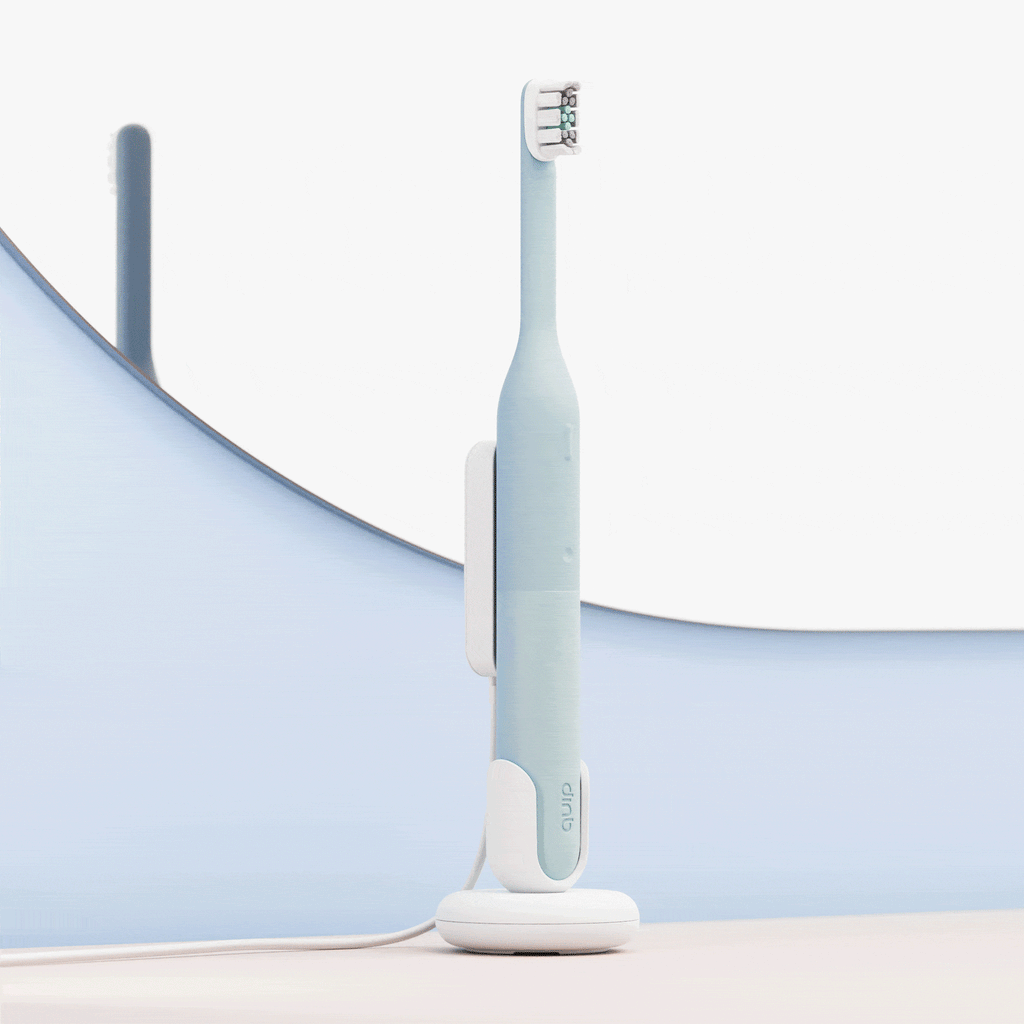 A minimalist light-blue electric toothbrush standing upright on a white charging base, set against a soft blue and white curved background.