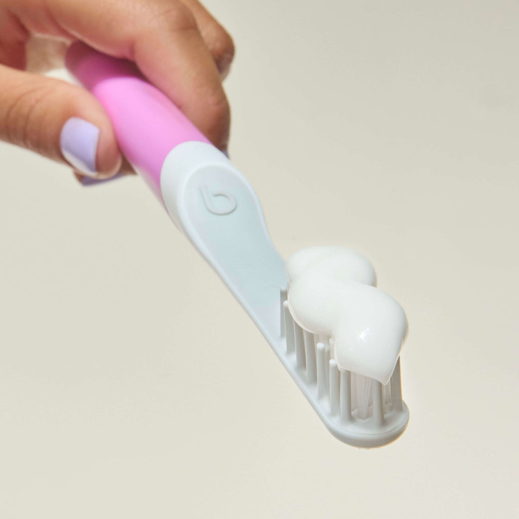 Hand holding a pink and white toothbrush against a plain background