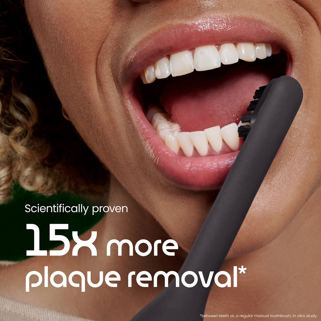 Close-up of a person brushing their teeth with a black toothbrush, emphasizing plaque removal benefits.